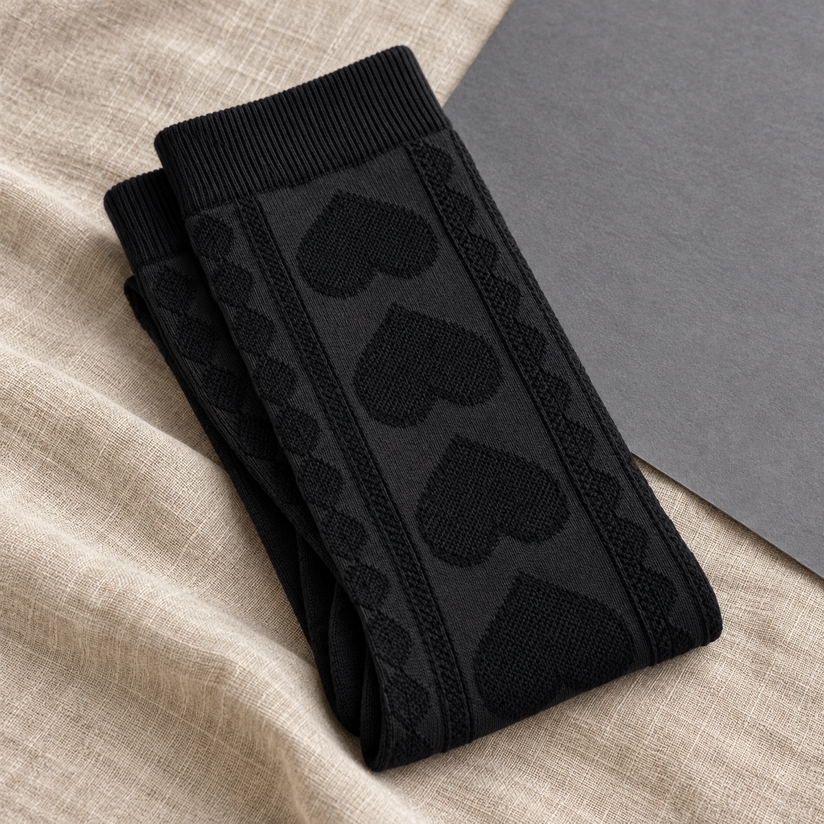 AI product illustration of Black socks folded on linen and slate paper, showing raised hearts and cable columns.