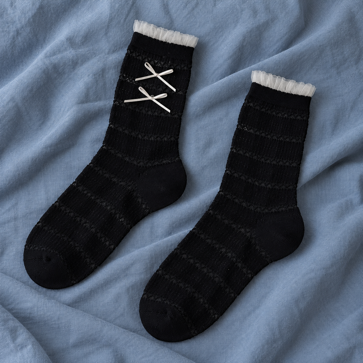 AI flat product illustration of a Black striped-knit sock pair with narrow tulle cuffs and two off-white bows on the observed face, on slate-blue cloth.