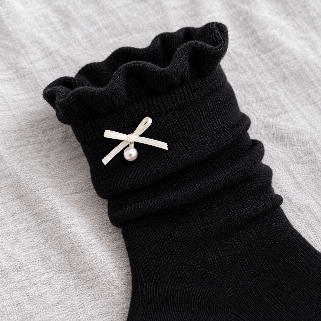 AI product illustration showing the rippled Black sock opening, narrow off-white ribbon bow and single pearl-style drop on gray cotton.