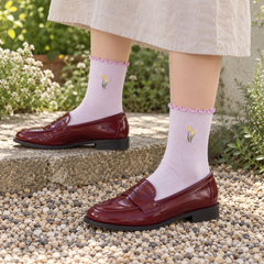 AI outdoor styling illustration of Lavender tulip ribbed socks with deep red loafers and an oat skirt on garden gravel.