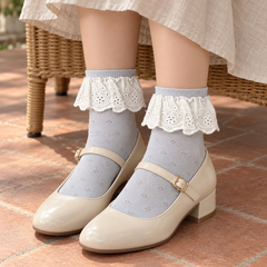 AI seated styling illustration of Light Blue eyelet-flounce socks with cream Mary Janes beside a wicker chair.