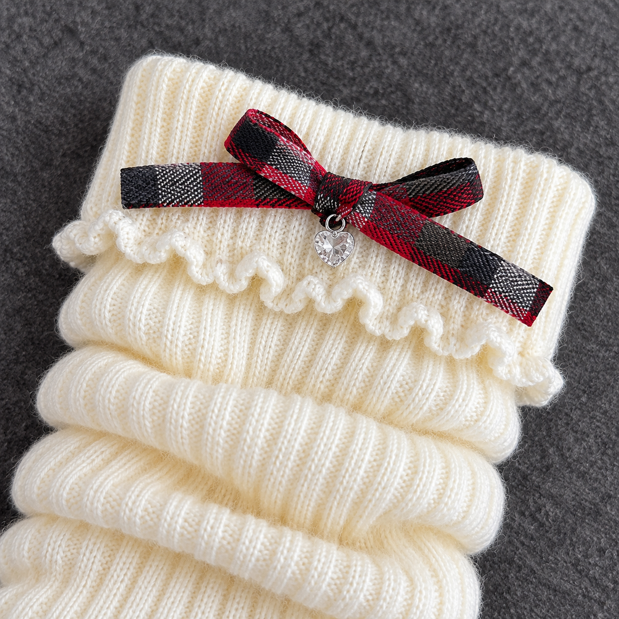 AI product detail of the red, black and gray plaid bow and clear heart charm on a White leg-warmer cuff.