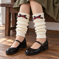 AI seated styling illustration of White plaid-bow footless leg warmers with black Mary Janes and an olive skirt.