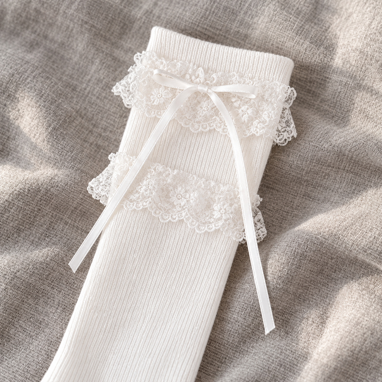 AI detail illustration of the White long sock's two separated floral lace bands, plain knit top and narrow ribbon tails on gray linen.