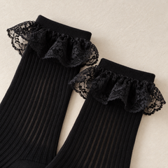 AI editorial illustration of Black ribbed sock cuffs with short plain knit lips above single gathered Black floral lace flounces.