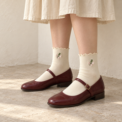 AI standing outfit illustration of Lettuce-Edge White floral-sprig socks with burgundy Mary Janes beside a cream wall.