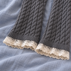 AI detail illustration of open lower edges of Dark Gray cable-knit leg warmers with narrow rib bands and cream scalloped floral lace.