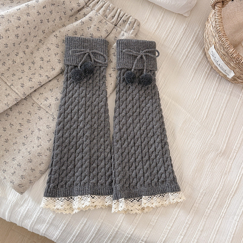 Untouched original reference of a Dark Gray footless cable-knit leg warmer pair with foldover cuffs, yarn pompoms and cream lower lace.