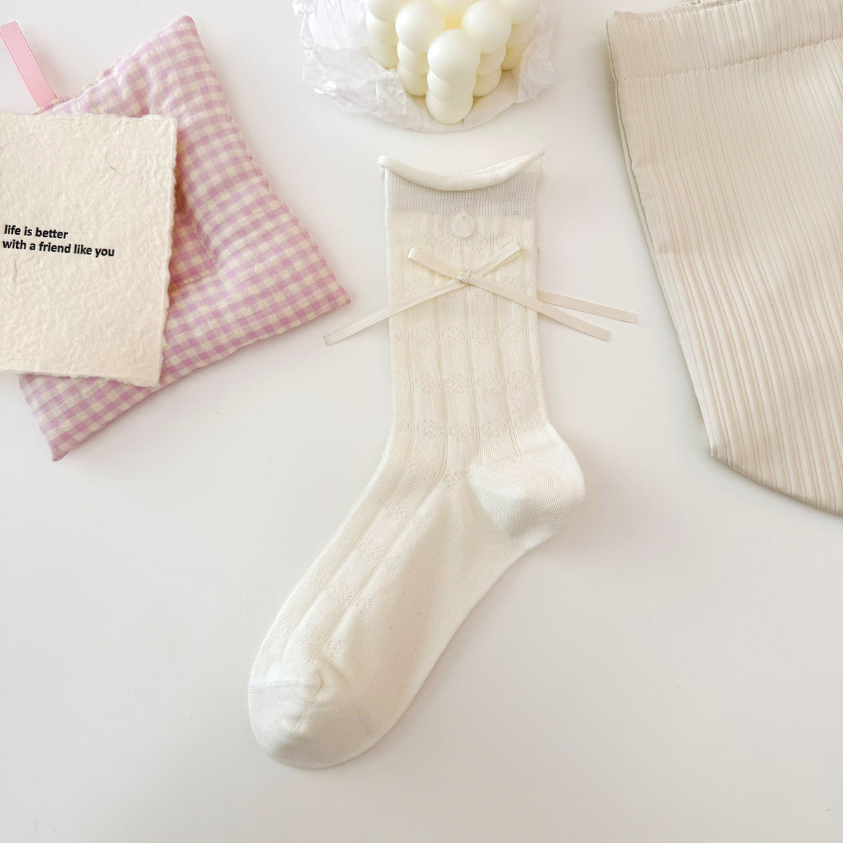 Cream Clover pattern pointelle crew sock with a rolled cuff, small round button and long ribbon bow.