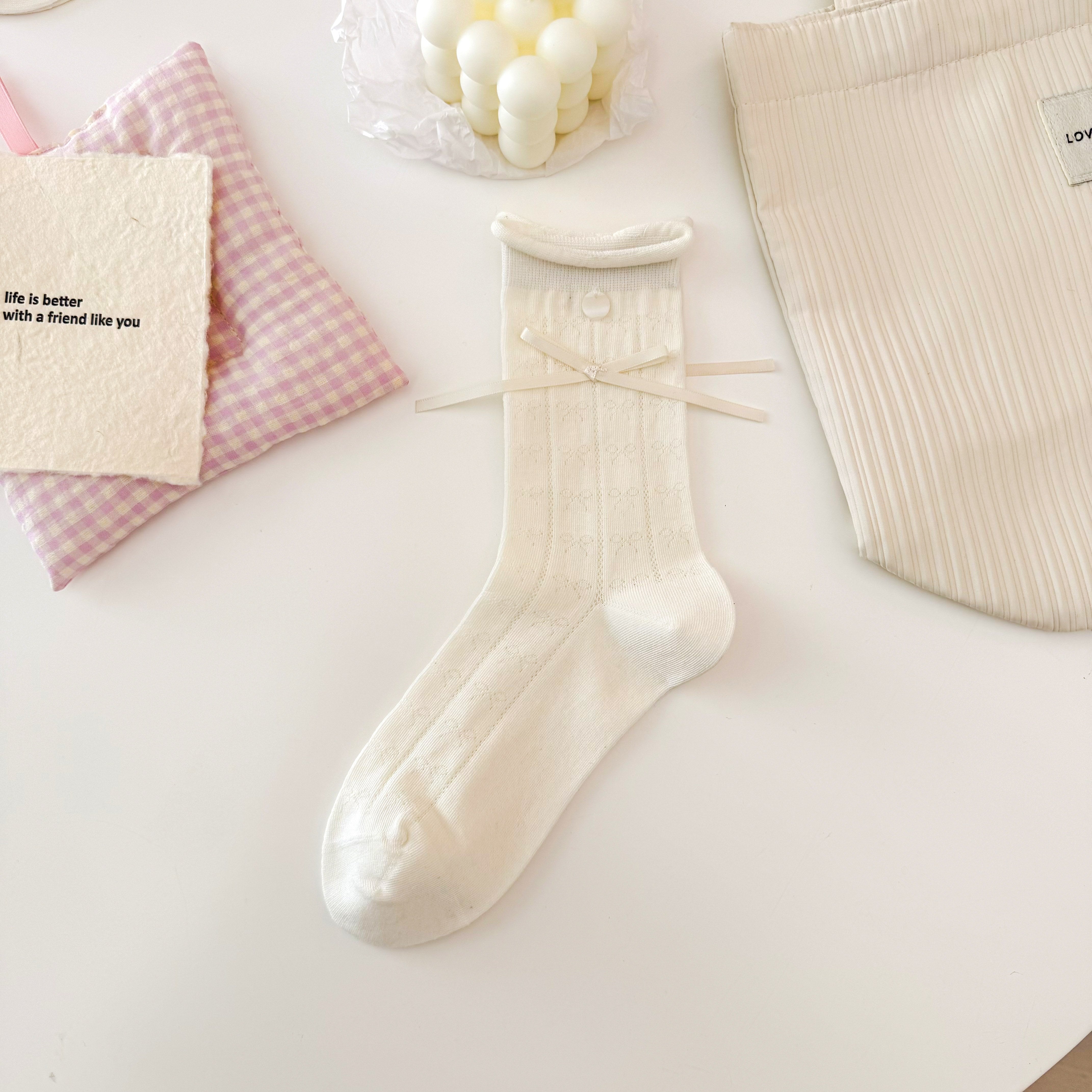 Cream Bow pattern crew sock with knitted bow motifs, a rolled cuff, round button and long ribbon bow.