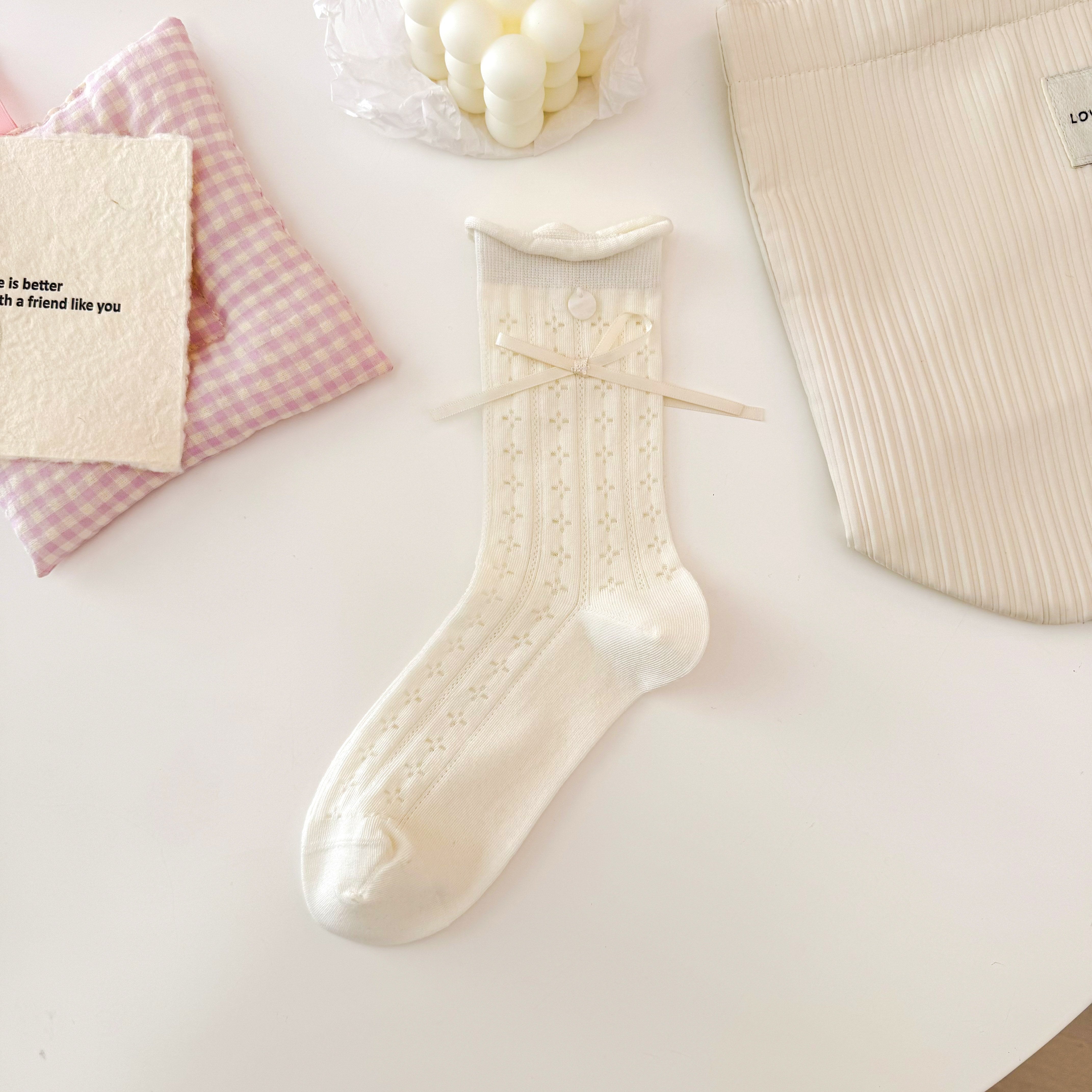 Cream Square pattern pointelle crew sock with small geometric openings, a rolled cuff, button and ribbon bow.