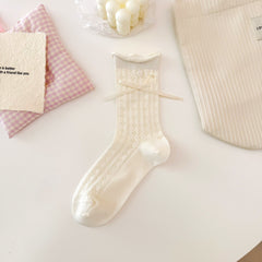 Cream Square pattern pointelle crew sock with small geometric openings, a rolled cuff, button and ribbon bow.