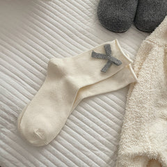 Cream socks with a gray knitted bow detail shown near one cuff