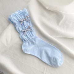 Blue knitted sock with two gray gingham bows and diagonal gathers above a plain foot