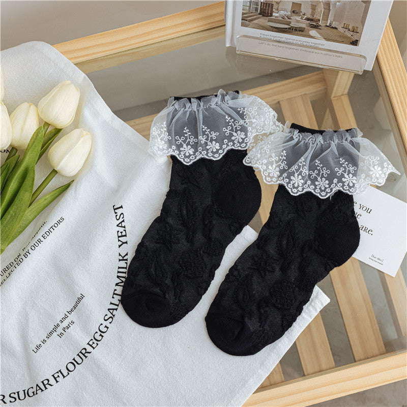 Black socks with raised star motifs and contrasting white floral lace cuffs, laid flat
